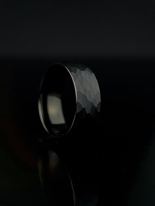 The Aether black tungsten ring featuring a hammered, light-catching faceted exterior.