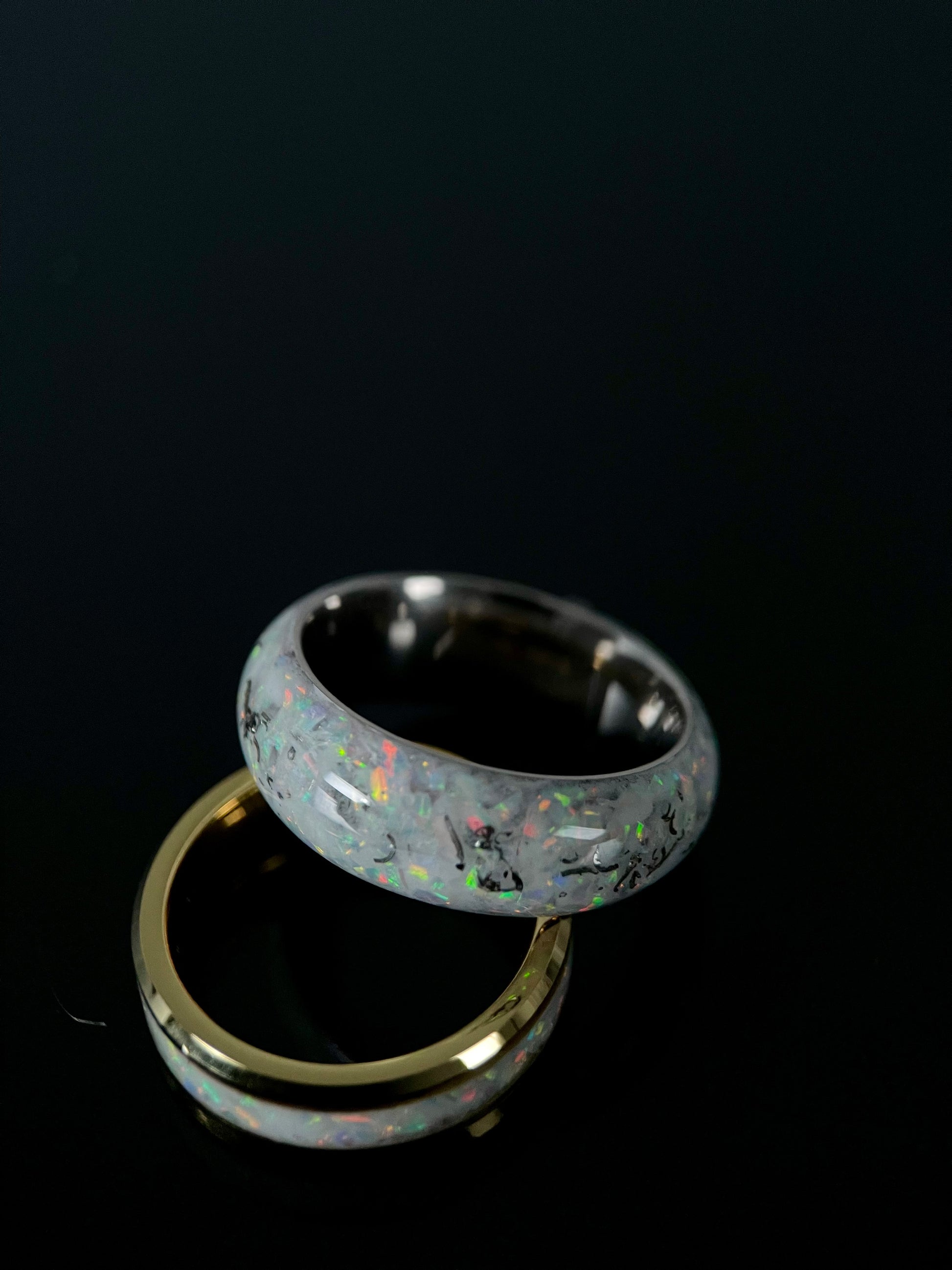 Close up of crushed meteorite and blue opal fragments creating a galaxy pattern on a black wedding ring.