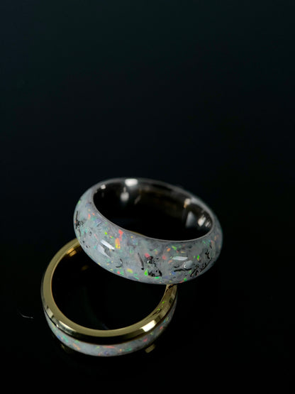Close up of crushed meteorite and blue opal fragments creating a galaxy pattern on a black wedding ring.