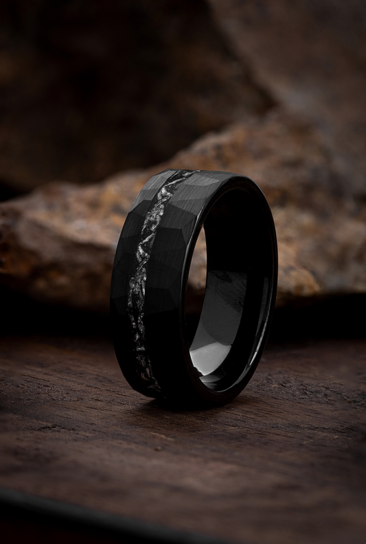 A black tungsten ring with a meteorite inlay, placed on a wooden surface.