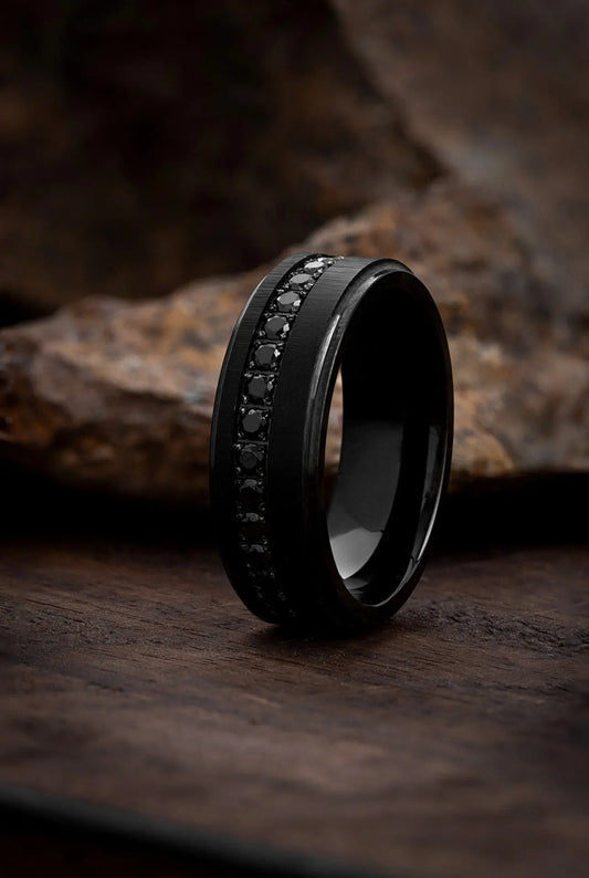 A matte black tungsten carbide ring with multiple jet-black cubic zirconia stones set around its circumference, displayed on a textured dark background.