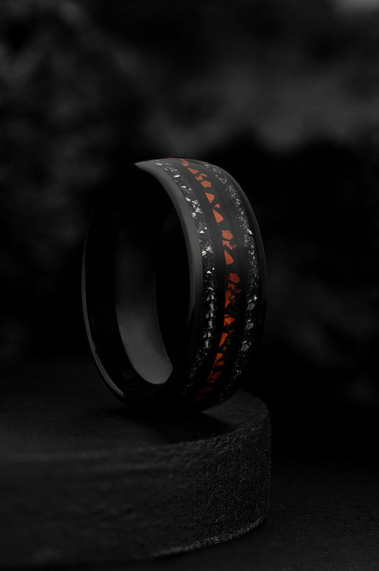 A ring with a tungsten core and dinosaur teeth embedded in the band, featuring a black and orange color scheme, displayed on a dark stand.