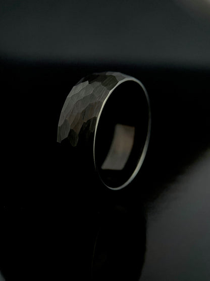 A black tungsten ring with a hammered surface, displayed against a dark background.