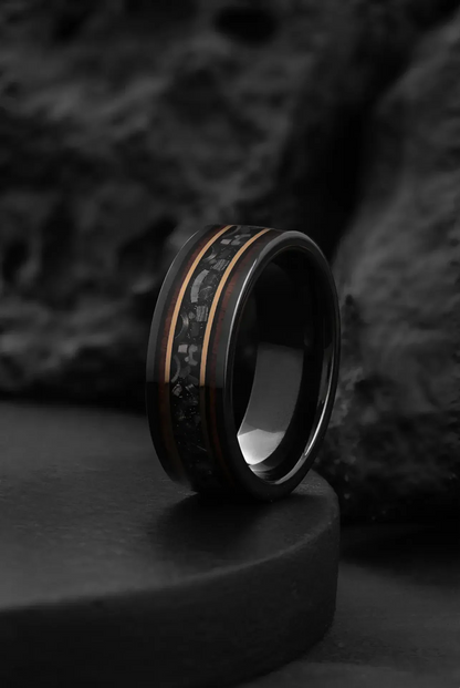 Black tungsten wedding band with meteorite chunks, polished silver interior, displayed on textured surface with dark background.