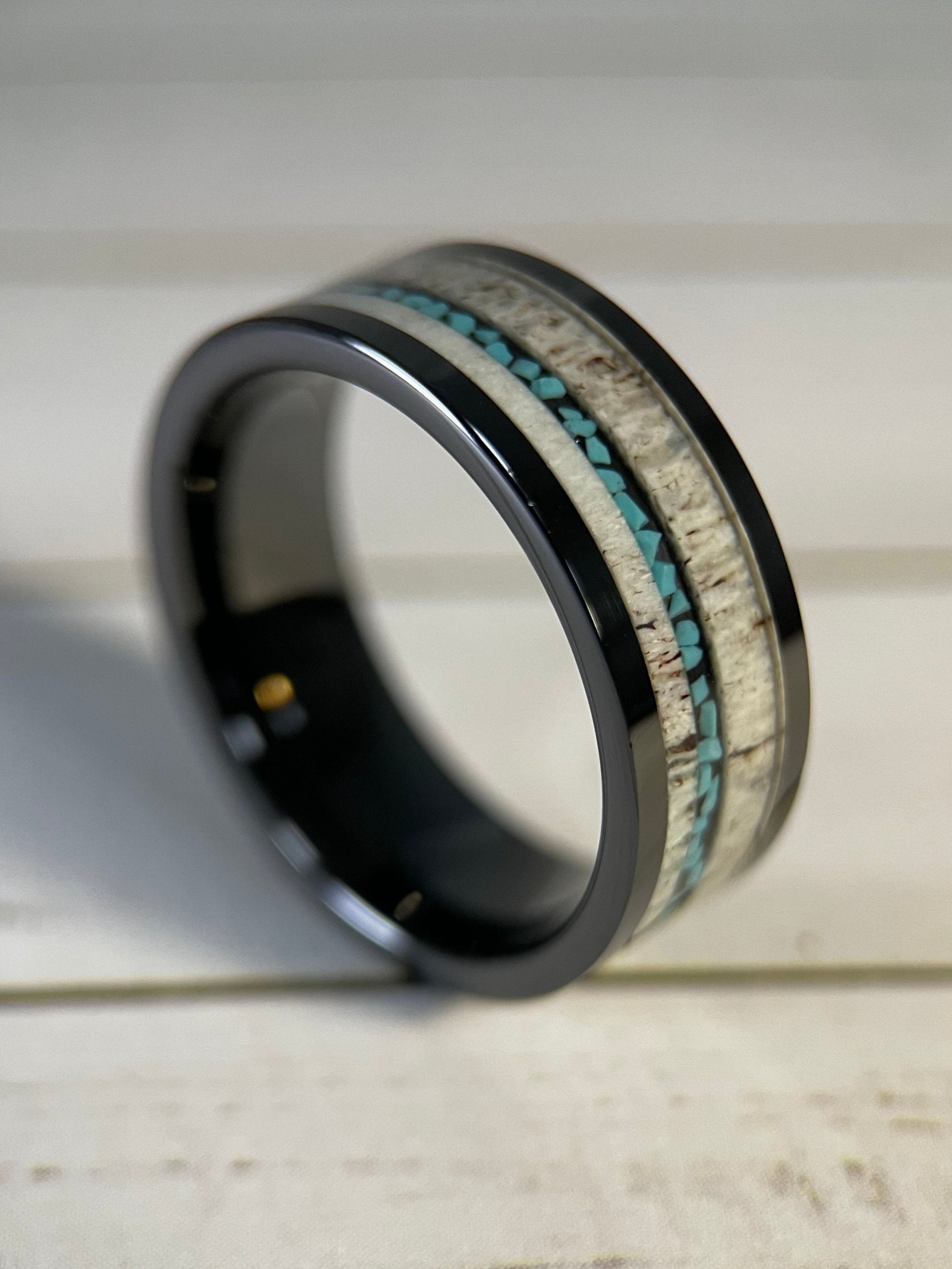 A black tungsten band ring with a inlay of deer antler and a vein of turquoise.