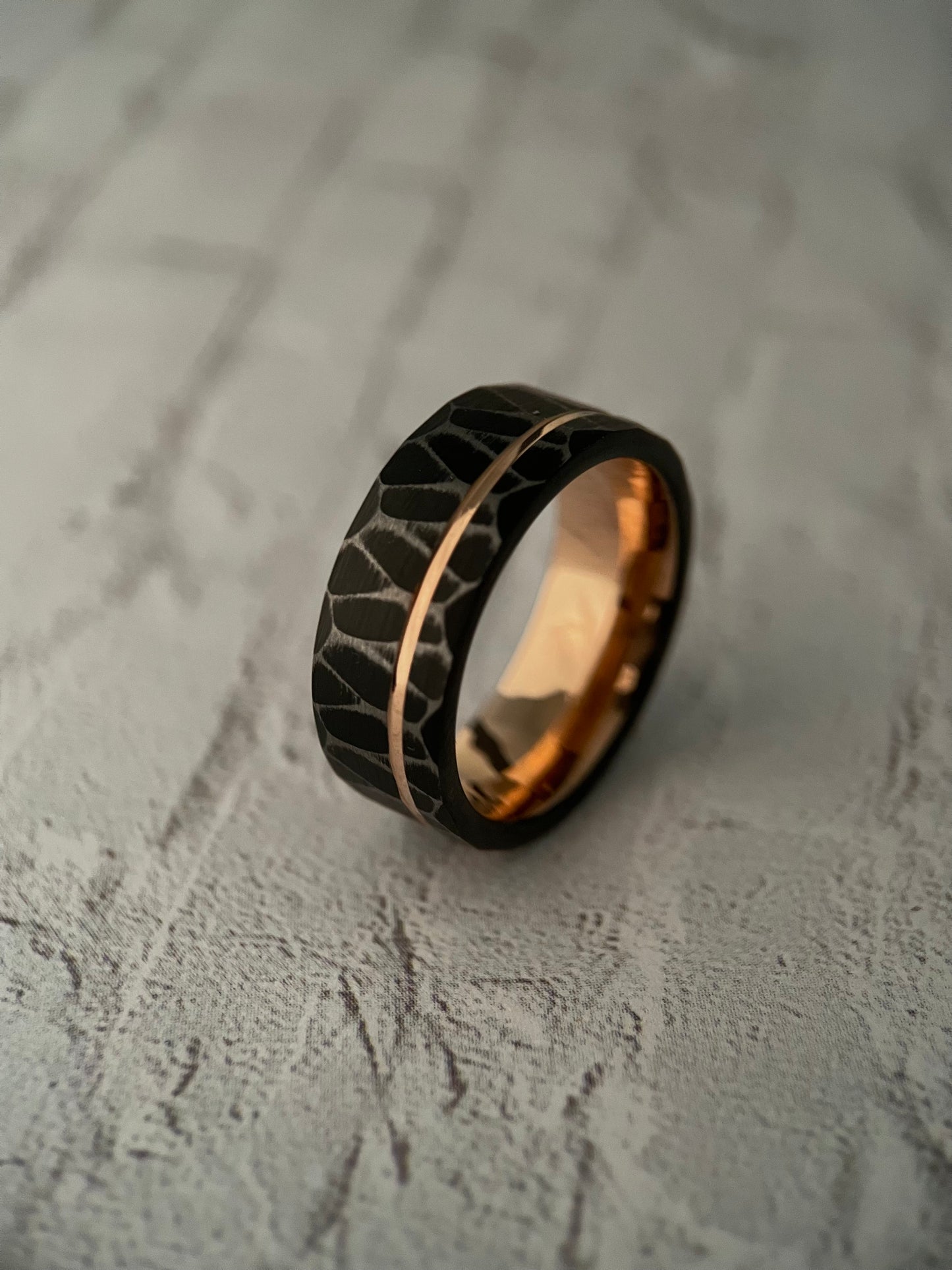The Vega black tungsten ring featuring a sharp faceted exterior and rose gold channel groove.