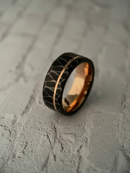 The Vega black tungsten ring featuring a sharp faceted exterior and rose gold channel groove.