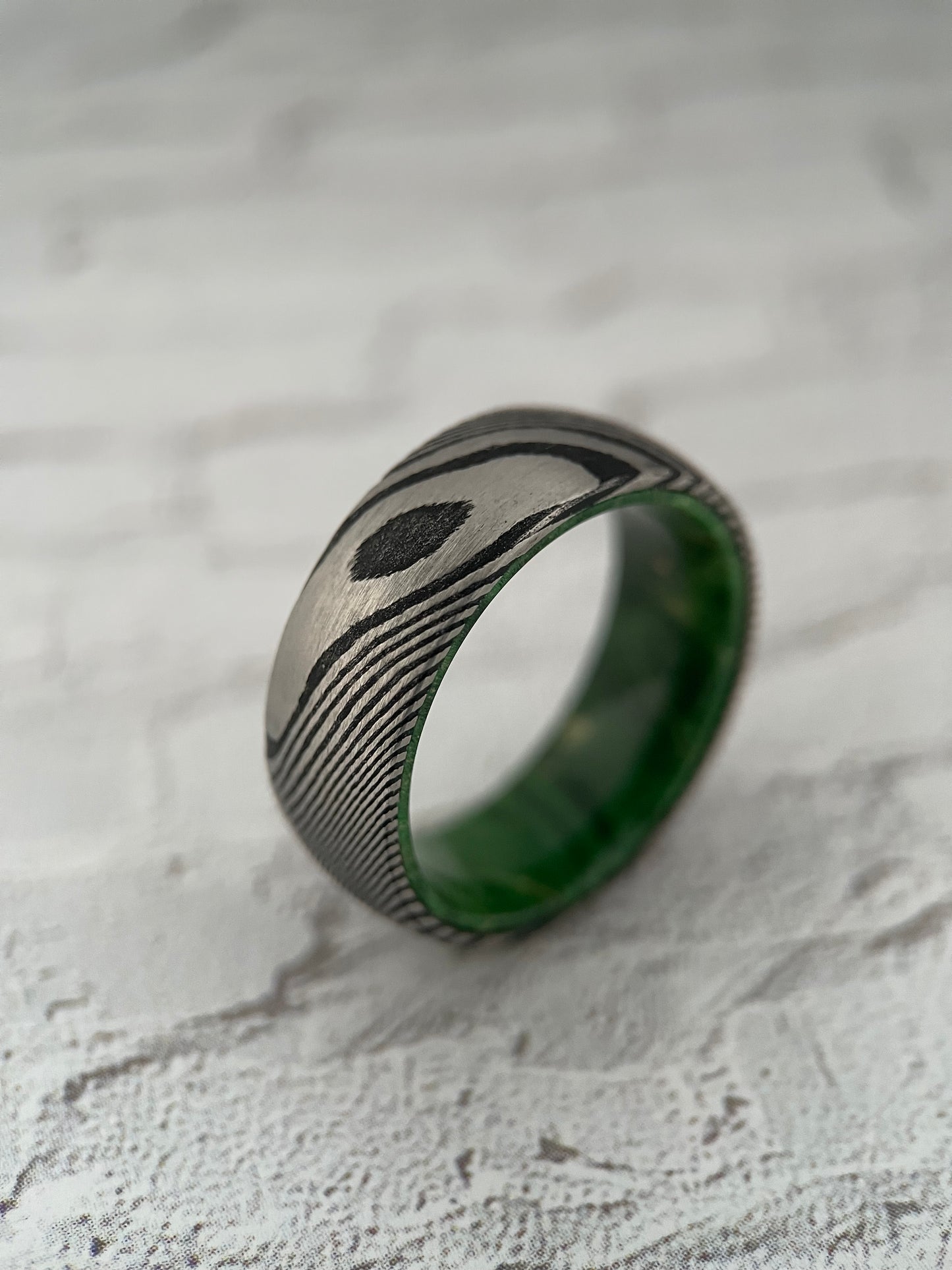 A Damascus steel ring with a green alder wood inner sleeve, featuring a distinctive pattern.