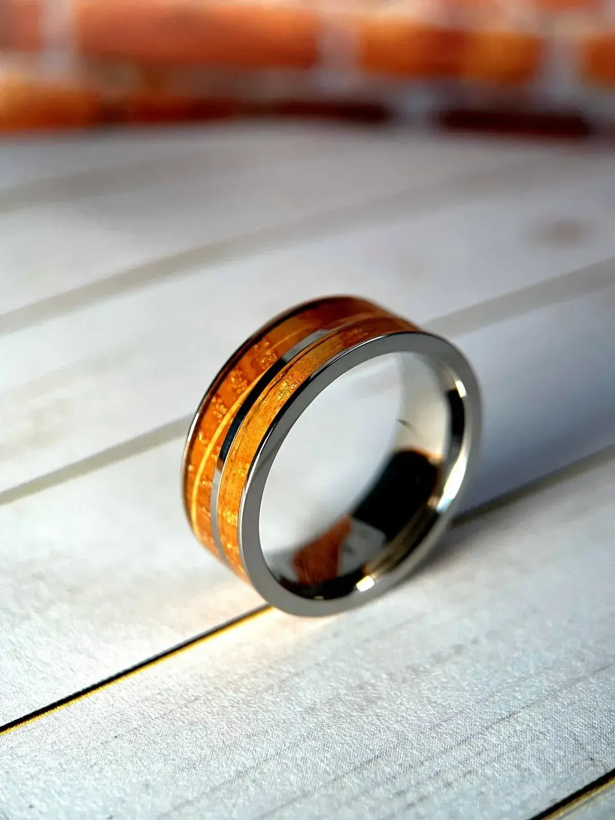 Whiskey barrel and titanium ring by Regalia Rings featuring reclaimed white oak inlay on a rustic wood background.