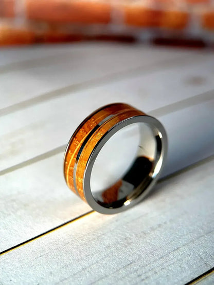 Whiskey barrel and titanium ring by Regalia Rings featuring reclaimed white oak inlay on a rustic wood background.